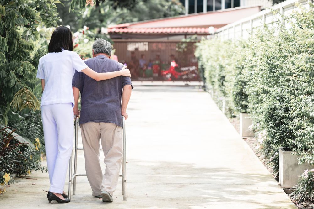 Two People Walking Arm-In-Arm Down a Sunny Garden Path — Home Nursing Services in Sutherland Shire, NSW