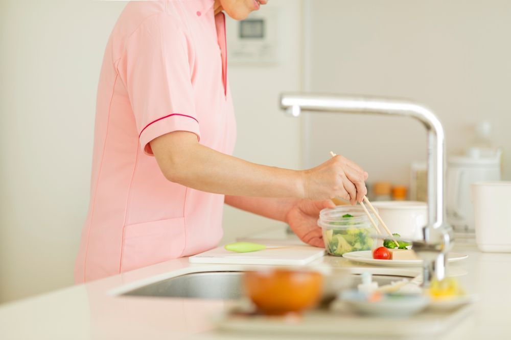 A Woman in a Pink Uniform is Preparing Food in a Kitchen — Home Nursing Services In Port Macquarie, NSW