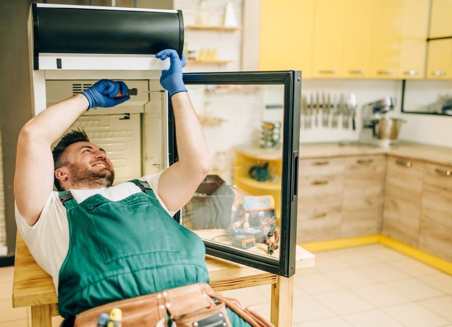 A Man is Fixing a Refrigerator in a Kitchen — Home Nursing Services in Wauchope, NSW