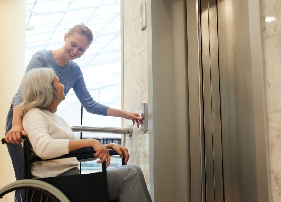 A Woman Is Helping an Elderly Woman in A Wheelchair — Home Nursing Services in Wauchope, NSW