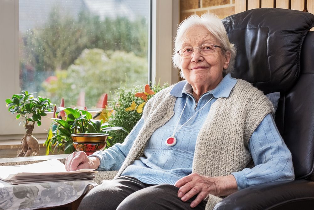 An Elderly Woman Is Sitting in A Chair in Front of A Window — Home Nursing Services in Kew, NSW