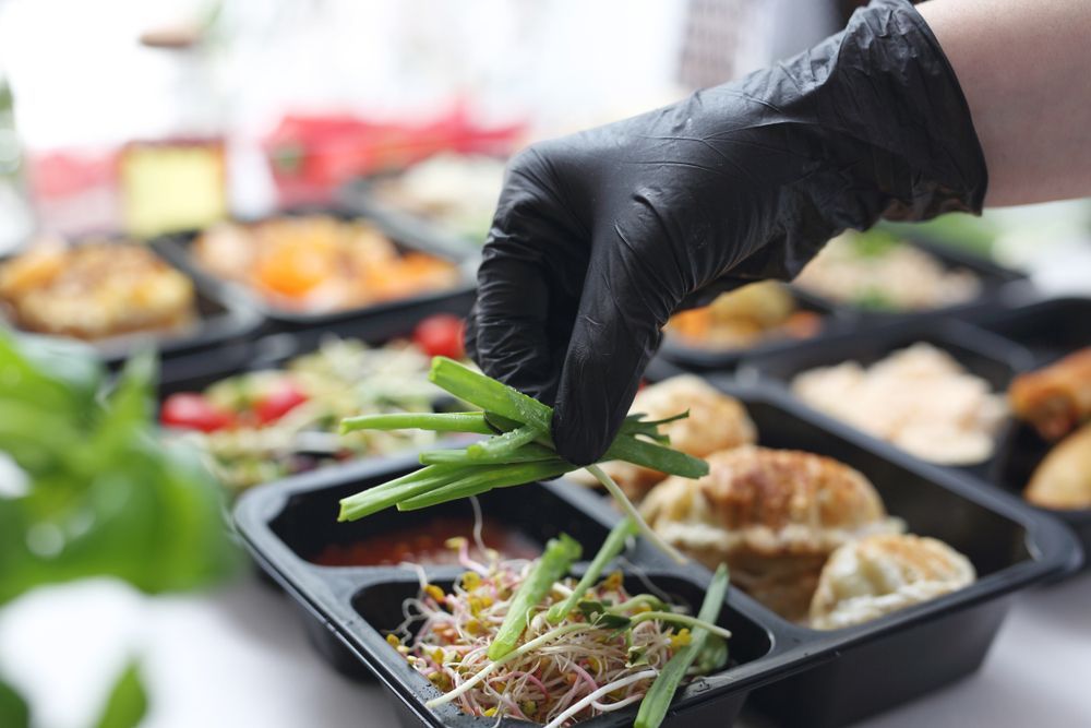 Gloved Hand Placing Green Vegetables Into Meal Prep Containers — Home Nursing Services in Hurstville, NSW