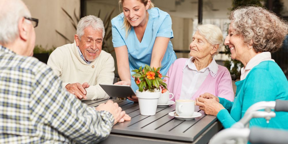 Caregiver Showing a Tablet to Four Older Adults Chatting Around — Home Nursing Services in Parramatta, NSW