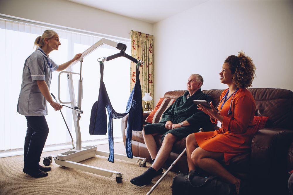 A Nurse is Using a Lift to Lift an Elderly Man in a Living Room — Home Nursing Services In Port Macquarie, NSW