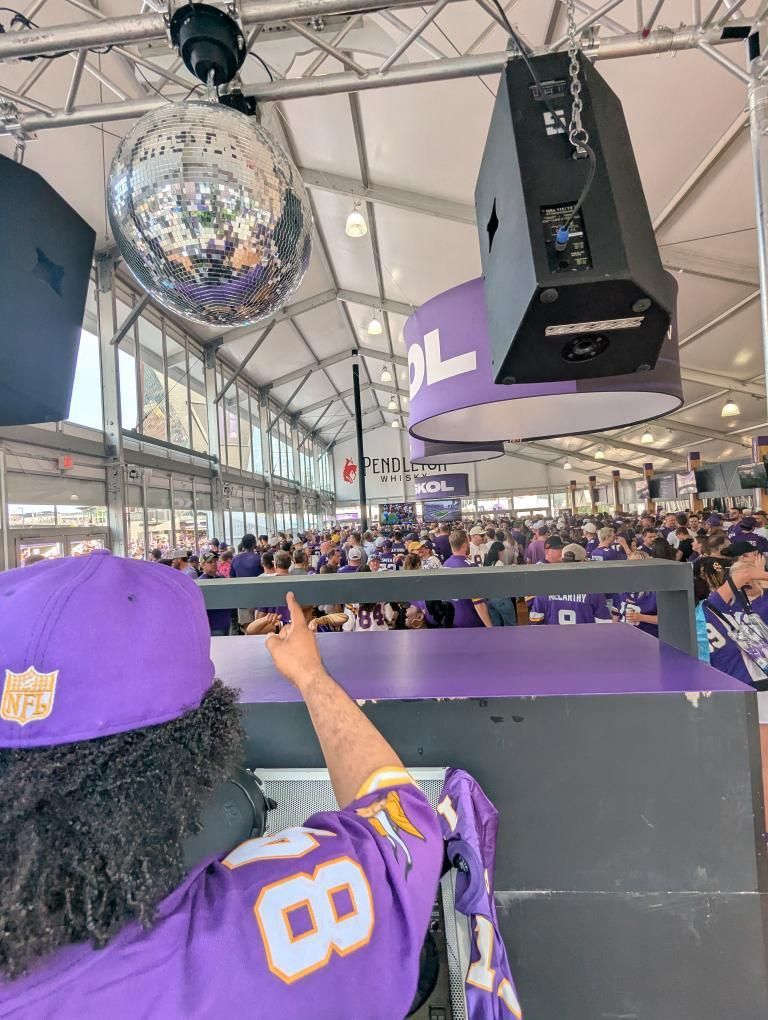 Purple-clad fan cheering at a crowded indoor event beneath a disco ball
