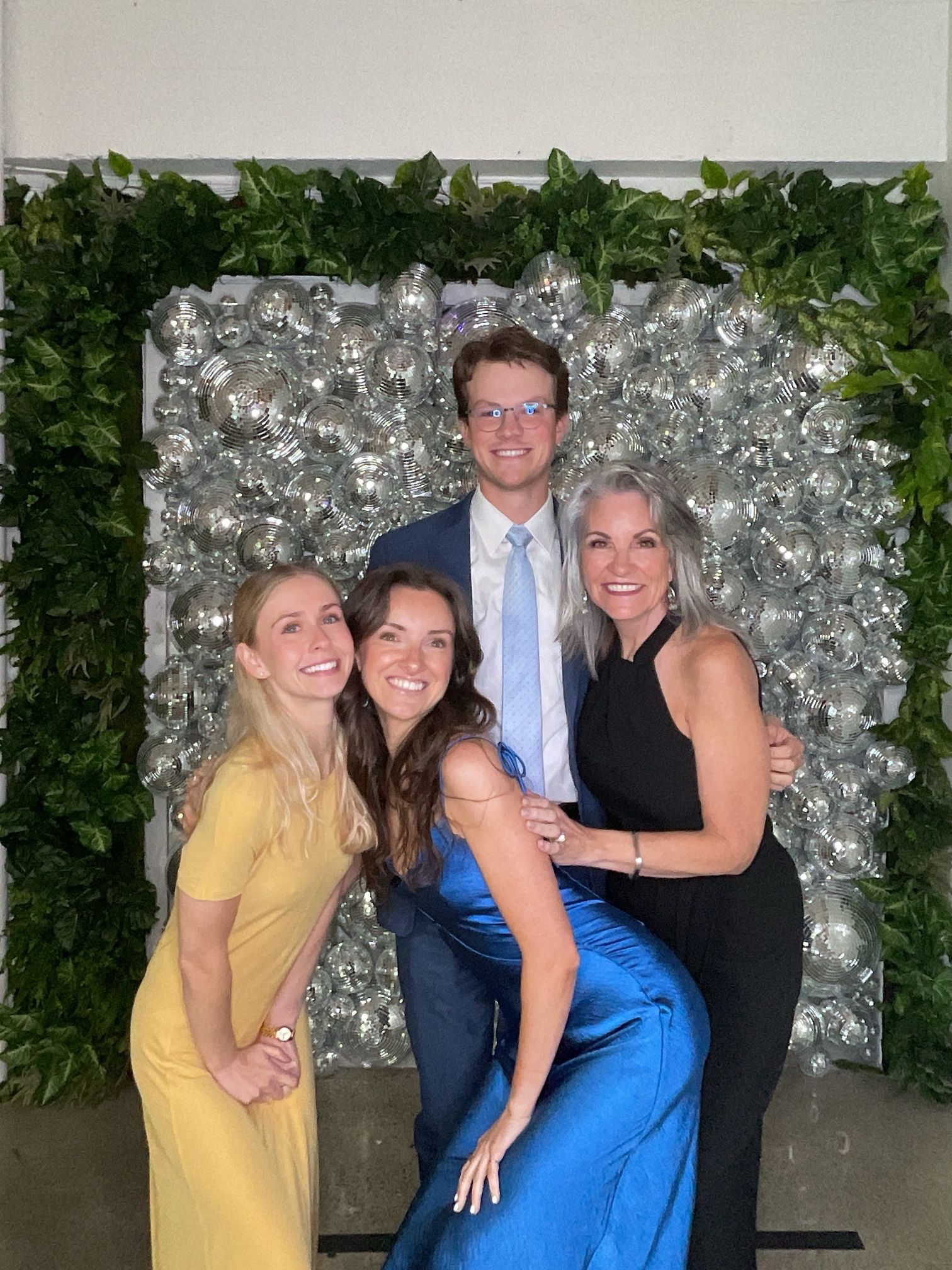 Four people posing together in front of a silver floral backdrop, smiling at an event.