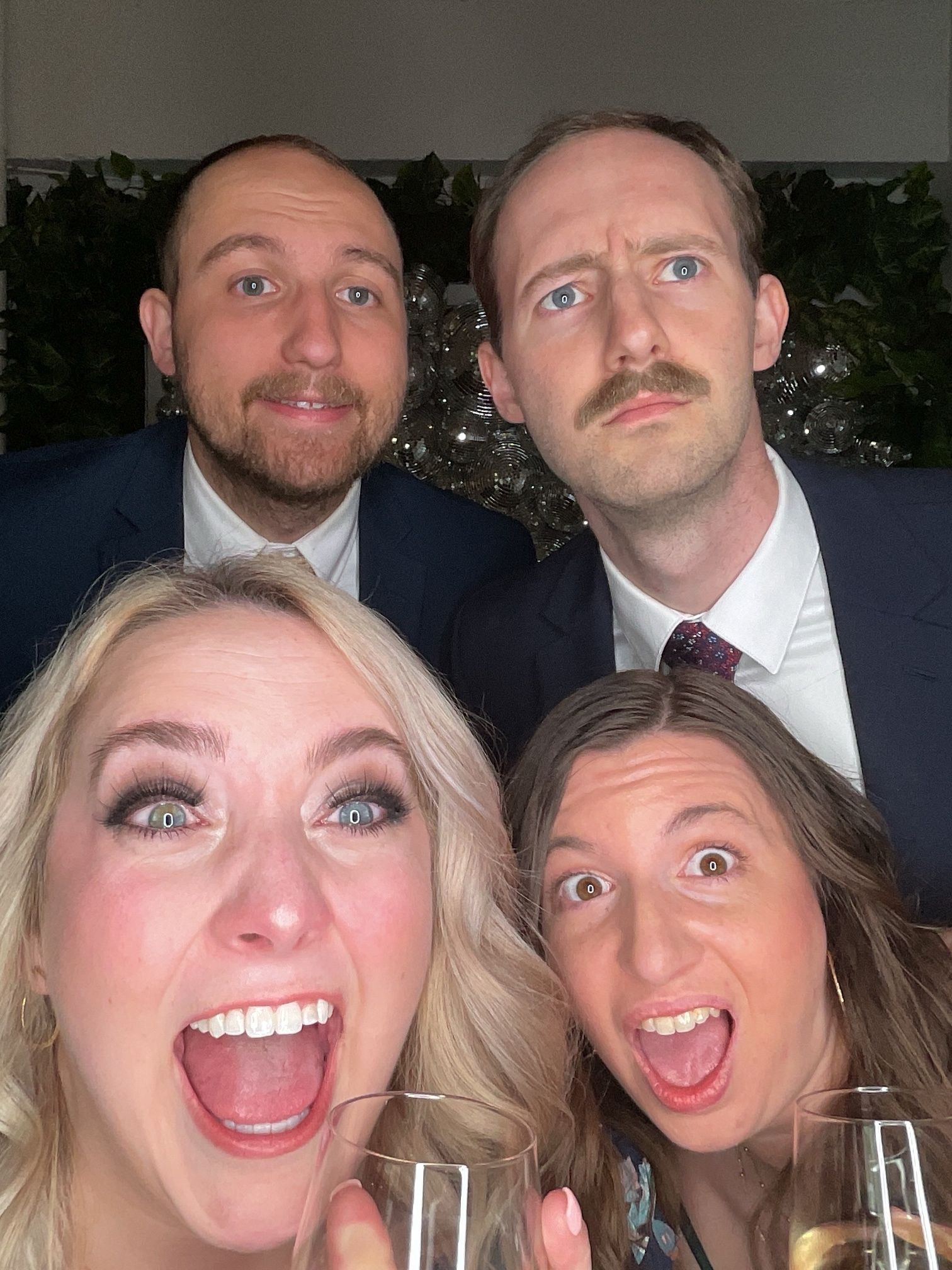Four people posing at a celebration, smiling with wide open mouths and holding champagne glasses.