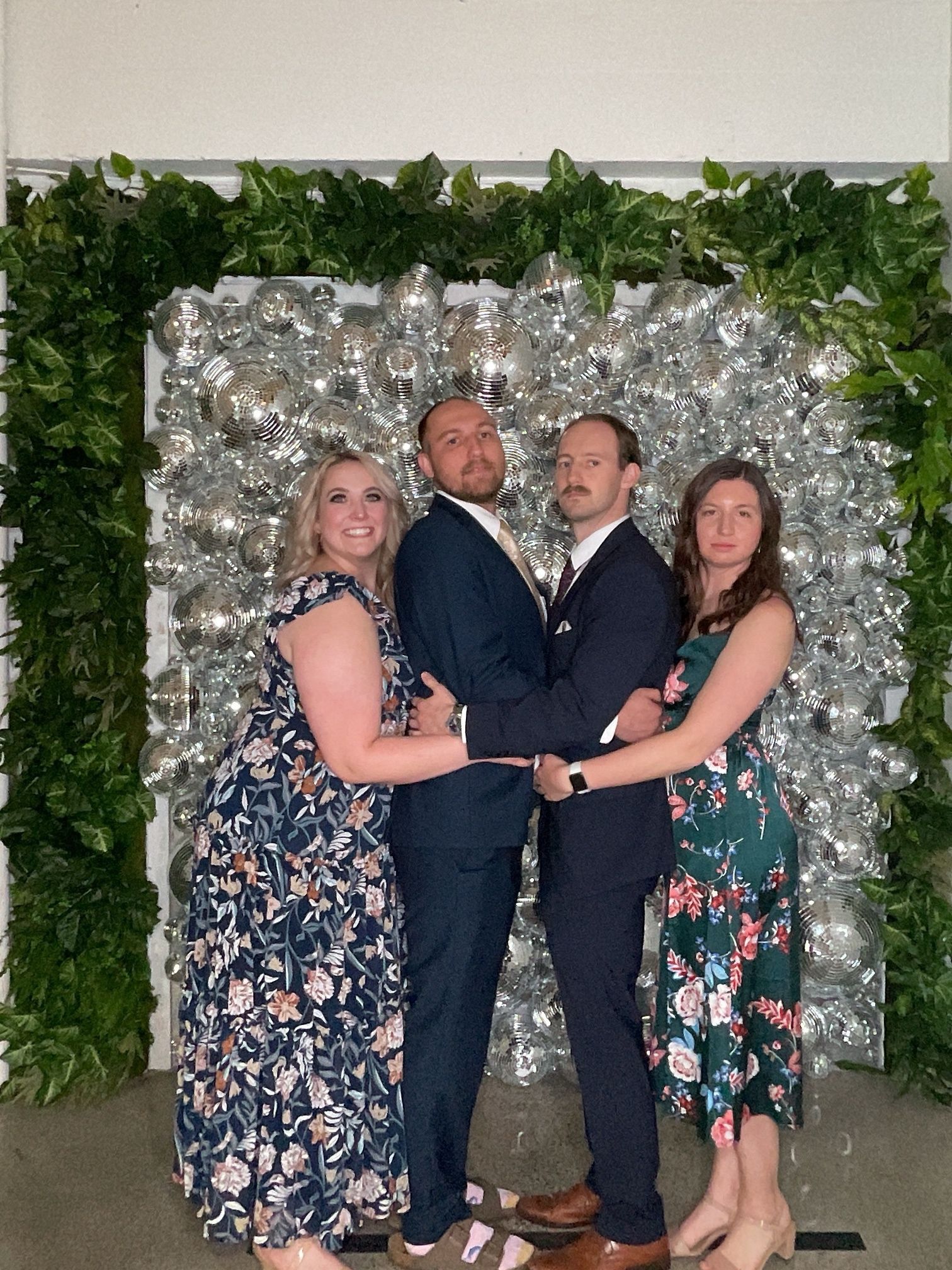 Four people posing together before a silver floral backdrop and greenery wall at a formal event