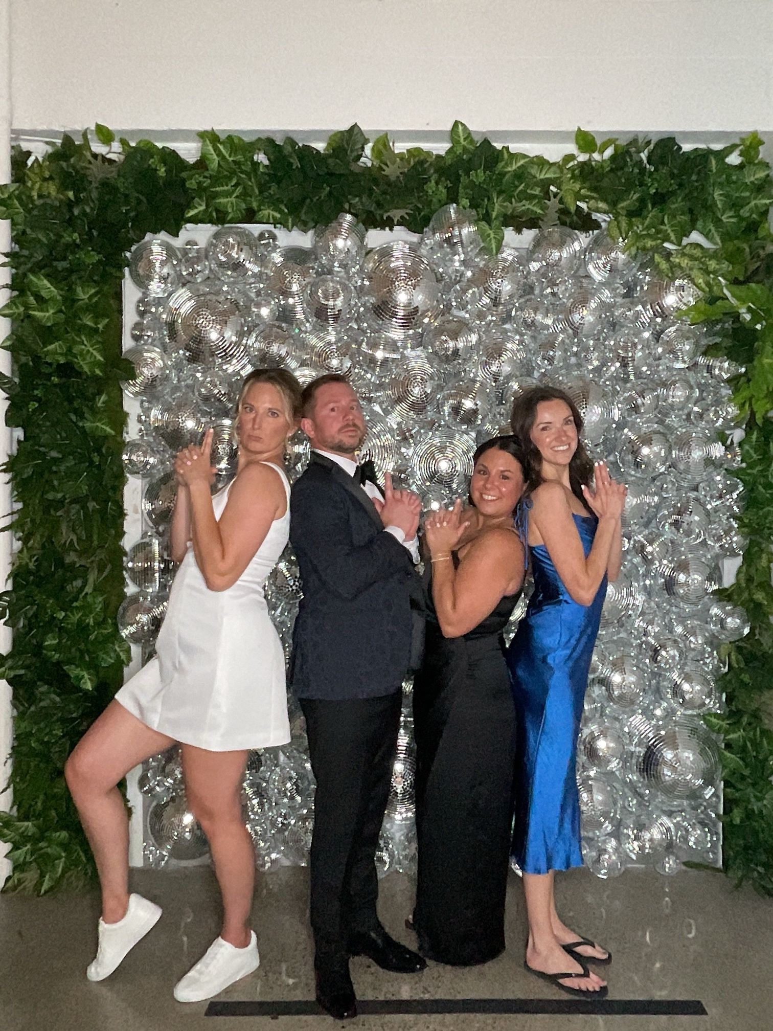 Four people posing in formal attire before a silver floral backdrop at a party.