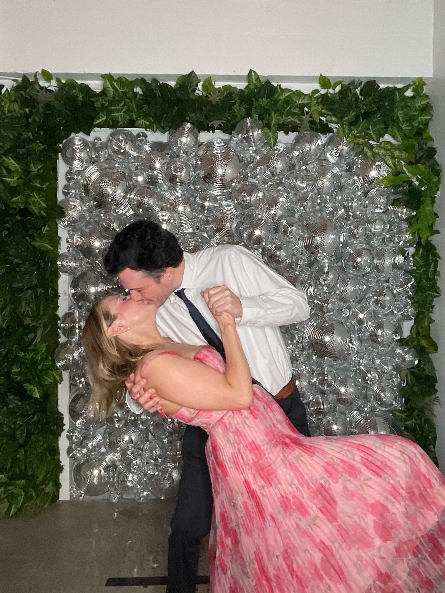 Couple dancing and kissing in front of a silver and green floral backdrop