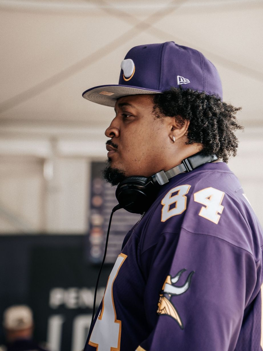 Purple-clad sports fan wearing #84 jersey and cap, standing indoors with headphones around neck