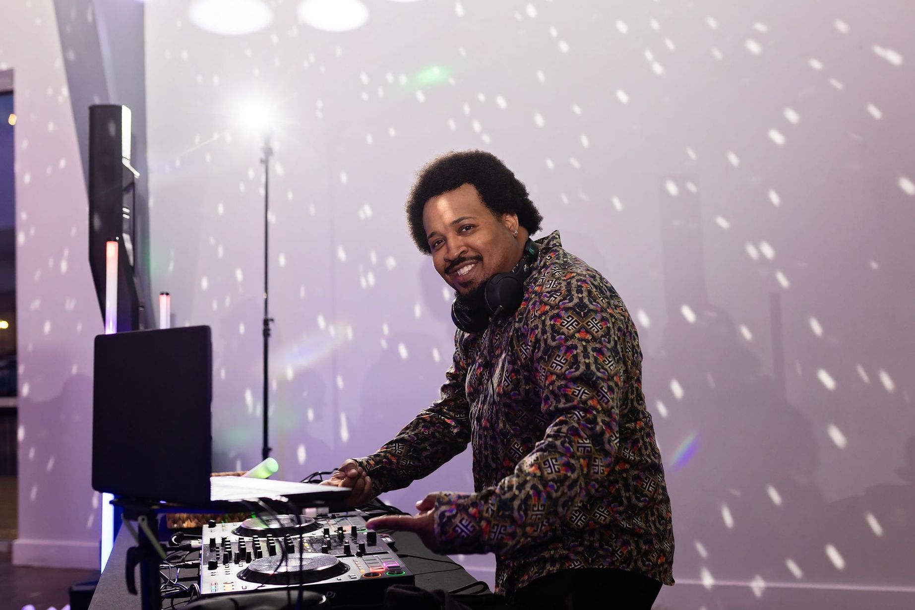 DJ at a turntable under purple stage lighting with a disco-ball pattern on the wall