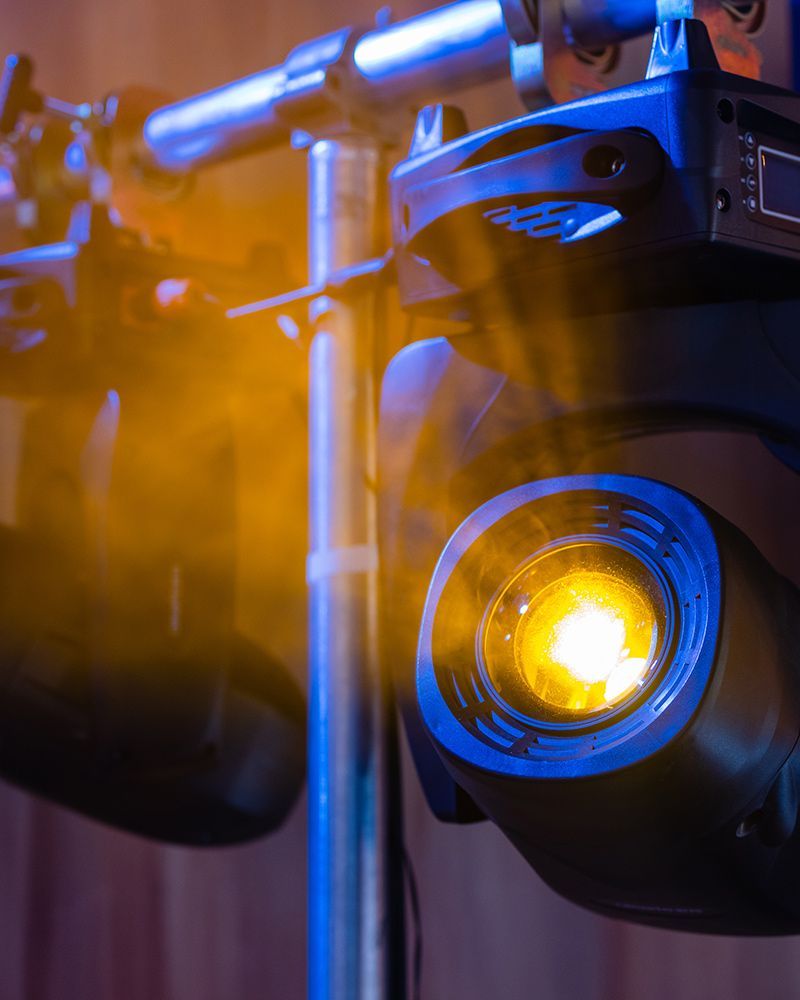 Black stage light with a bright yellow spotlight shining beside a metal truss.