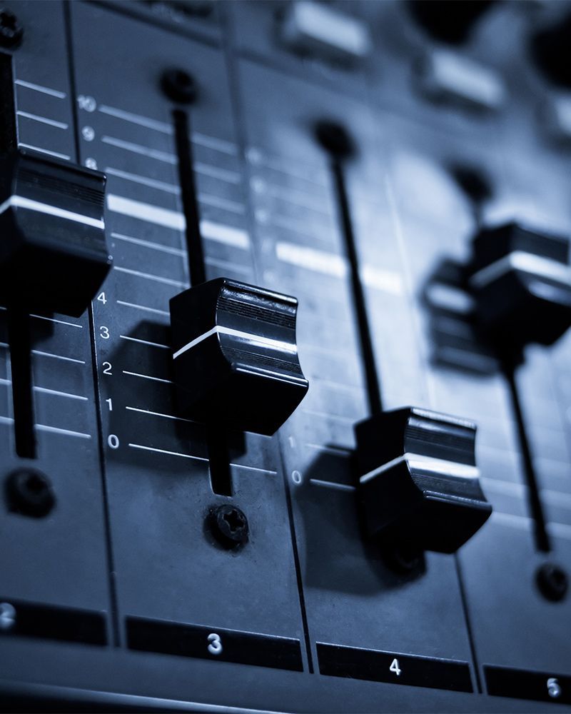 Close-up of black audio mixer sliders on a control panel with numbered tracks.