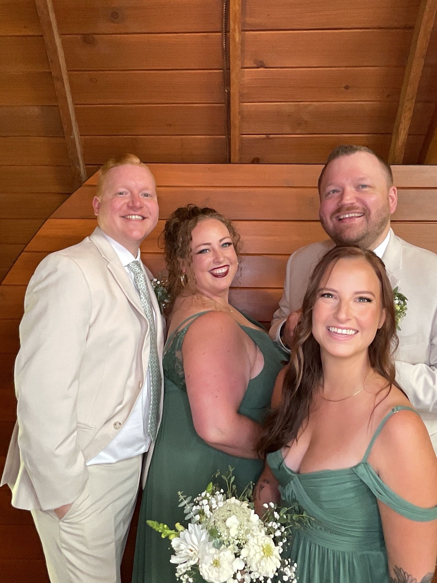Four people in formal attire posing on wooden stairs, smiling, with the women holding white bouquets.