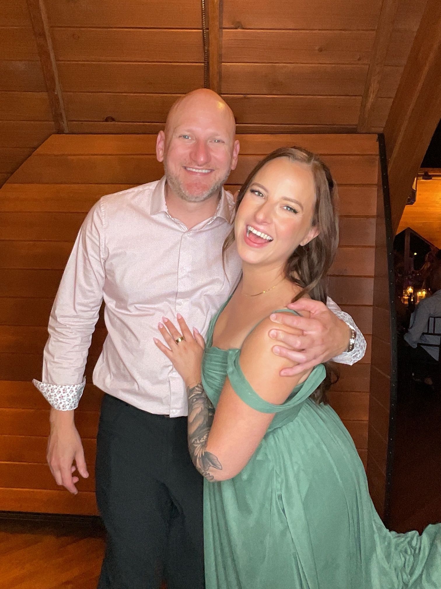 Smiling couple posing together on wooden stairs, with one wearing a mint green dress and the other a white shirt.