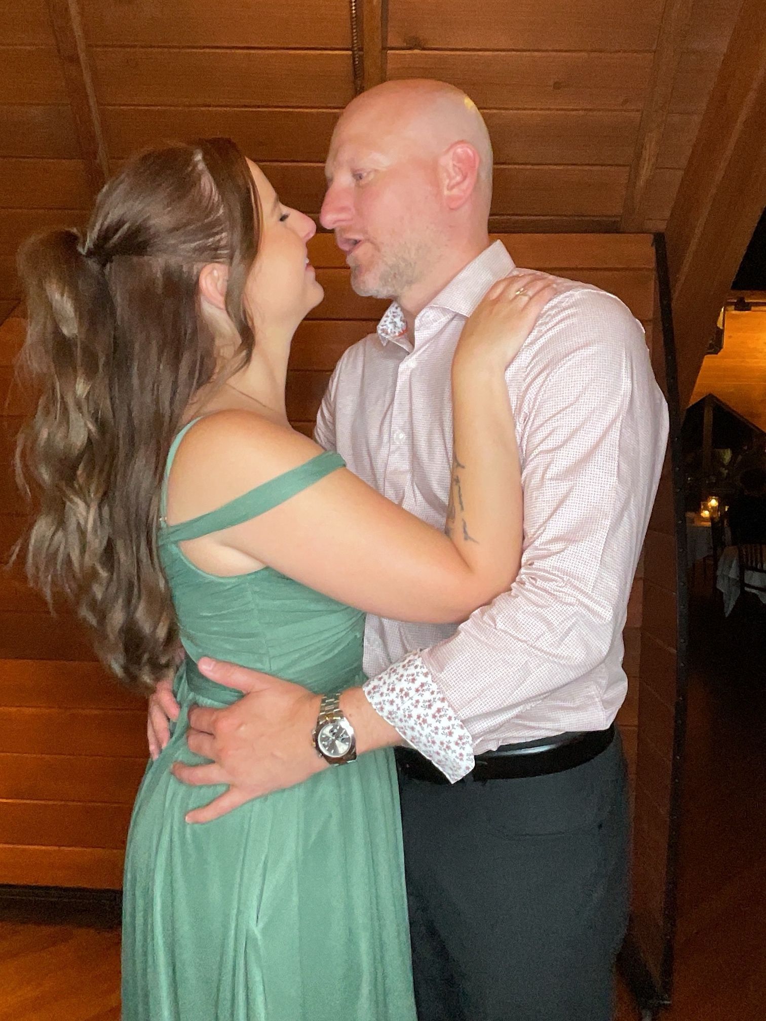 Couple embracing and smiling indoors, with a wooden staircase in the background
