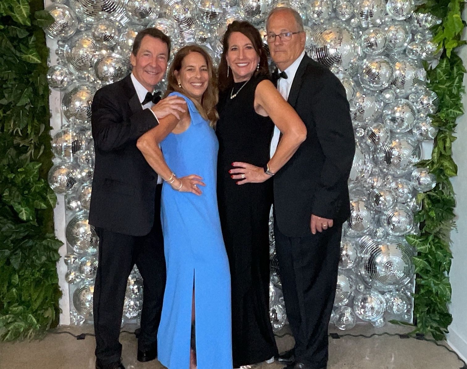 Four people posing in formalwear in front of a silver balloon backdrop