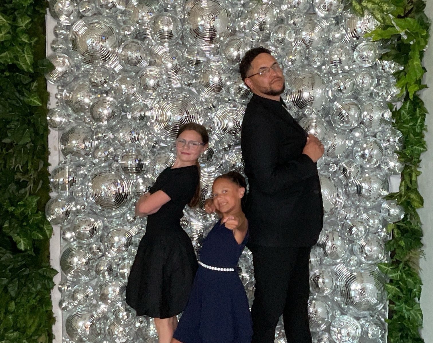 Three people posing before a shimmering silver wall with green foliage accents