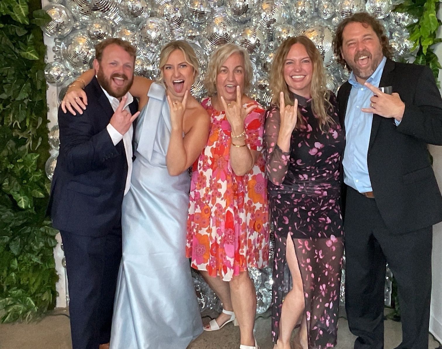 Five people in formal attire smiling and posing together at an indoor event.