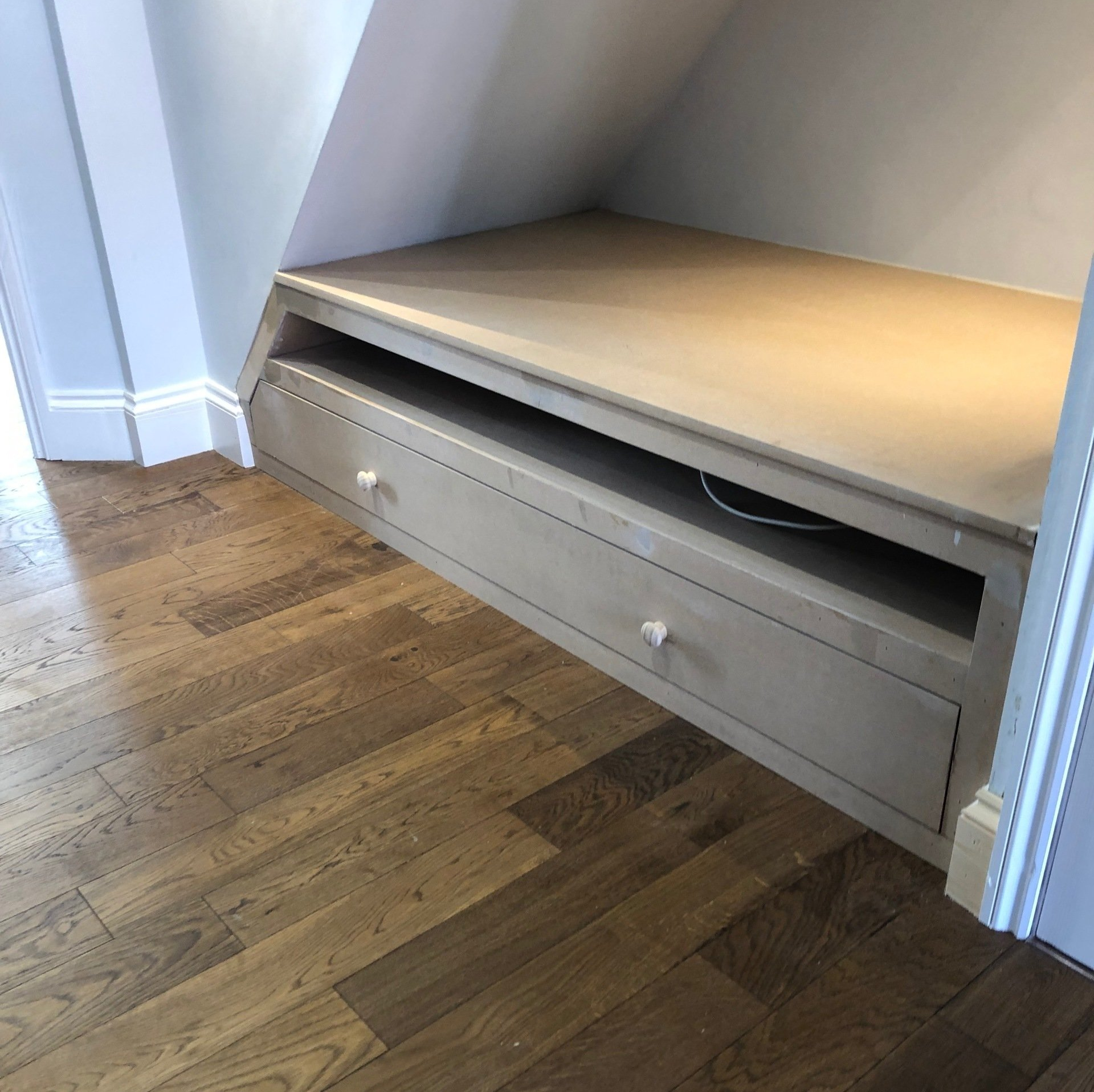 A wooden shelf with two drawers under a staircase.
