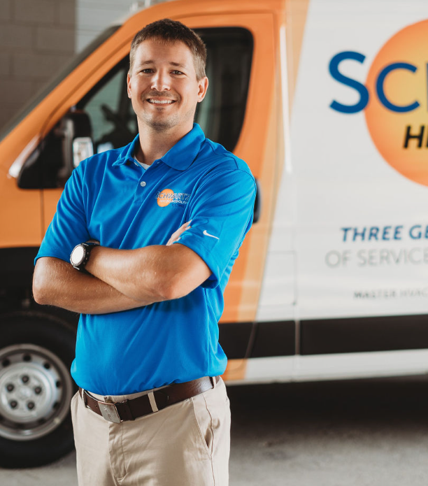 Smiling technician in blue polo stands with arms crossed beside a service van.