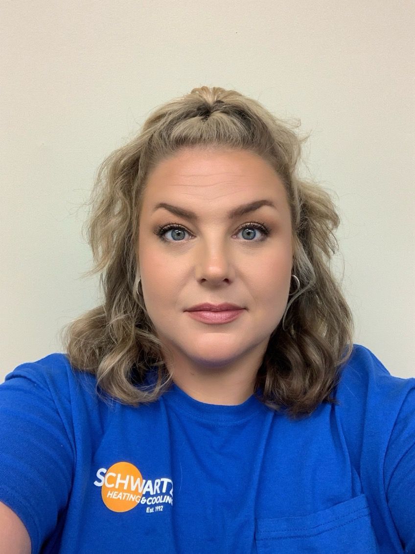 Woman in a bright blue shirt with a logo, facing the camera against a plain wall.