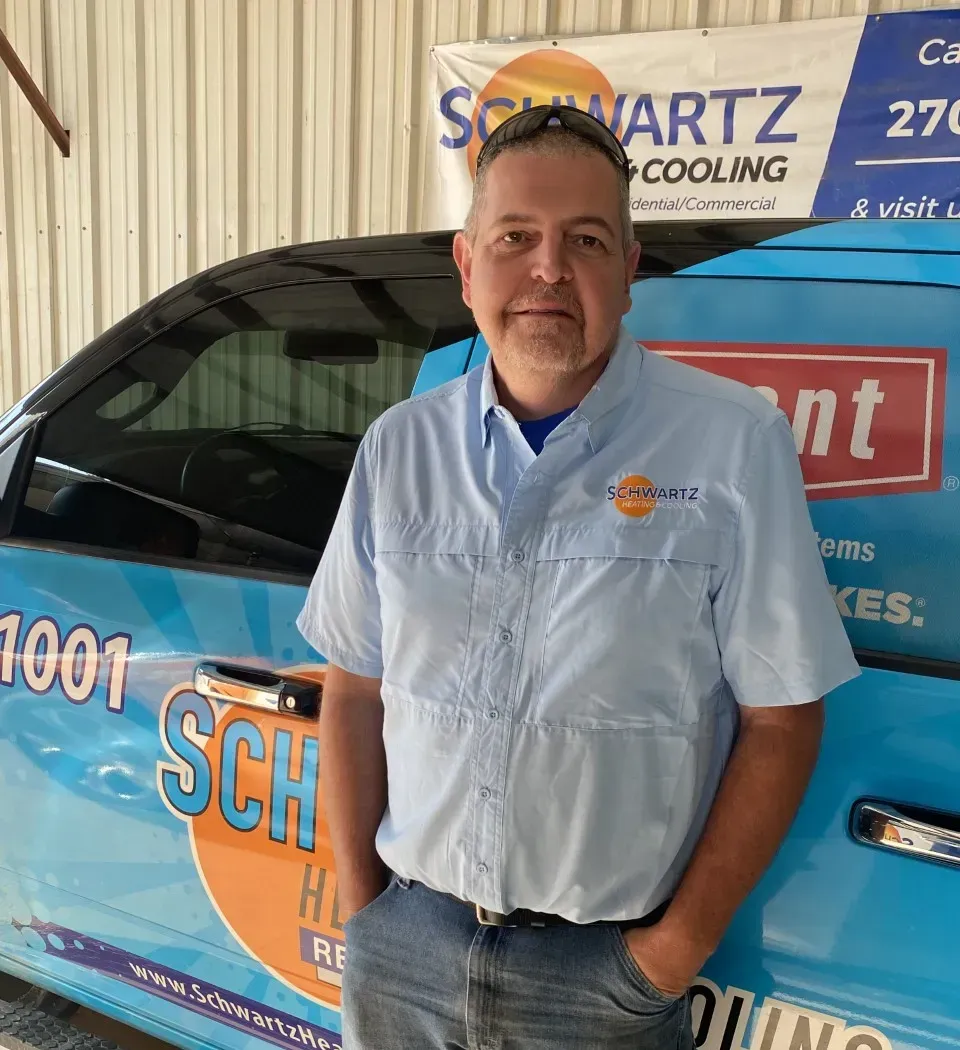 Man standing beside a blue service van with company logos in a garage setting