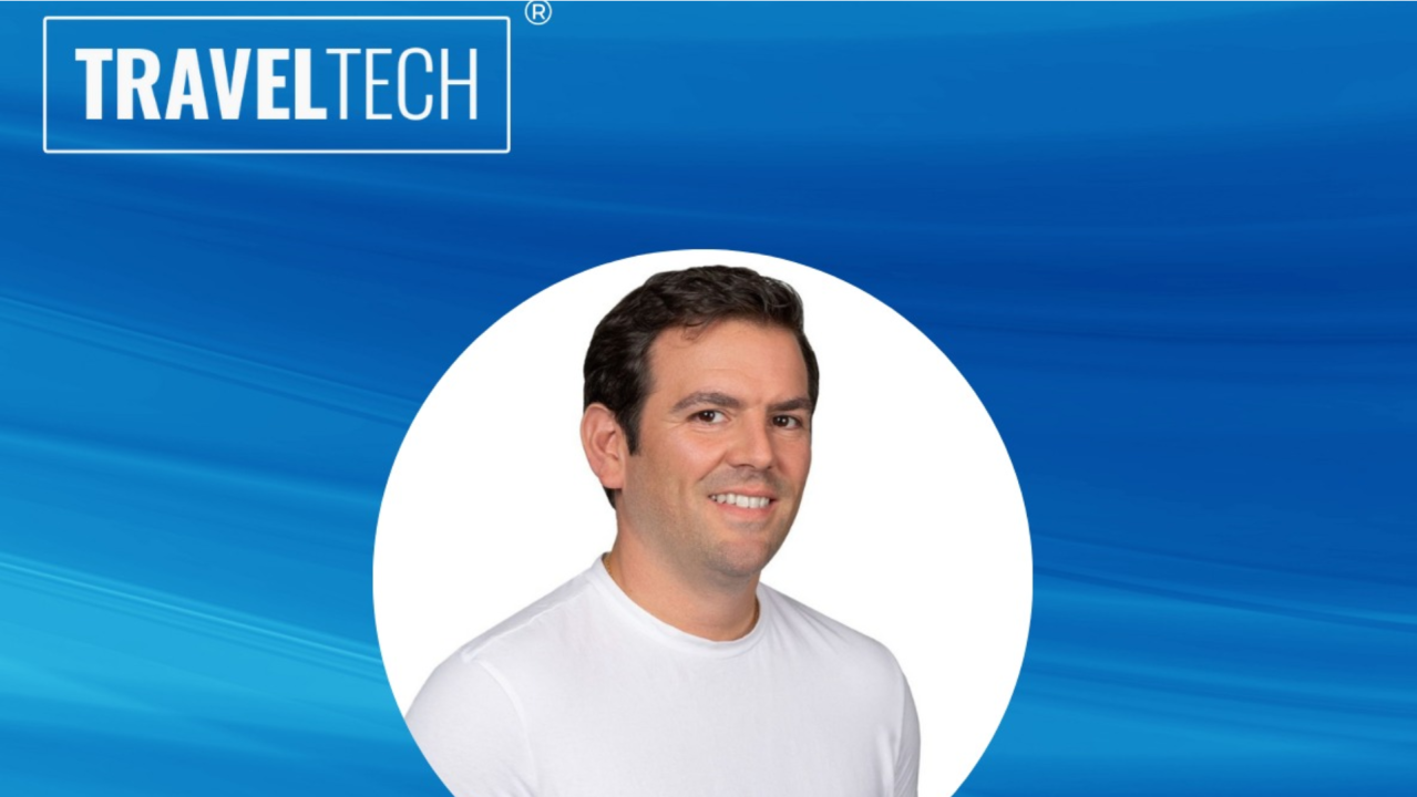 Um homem de camisa branca está sorrindo na frente de um logotipo da traveltech