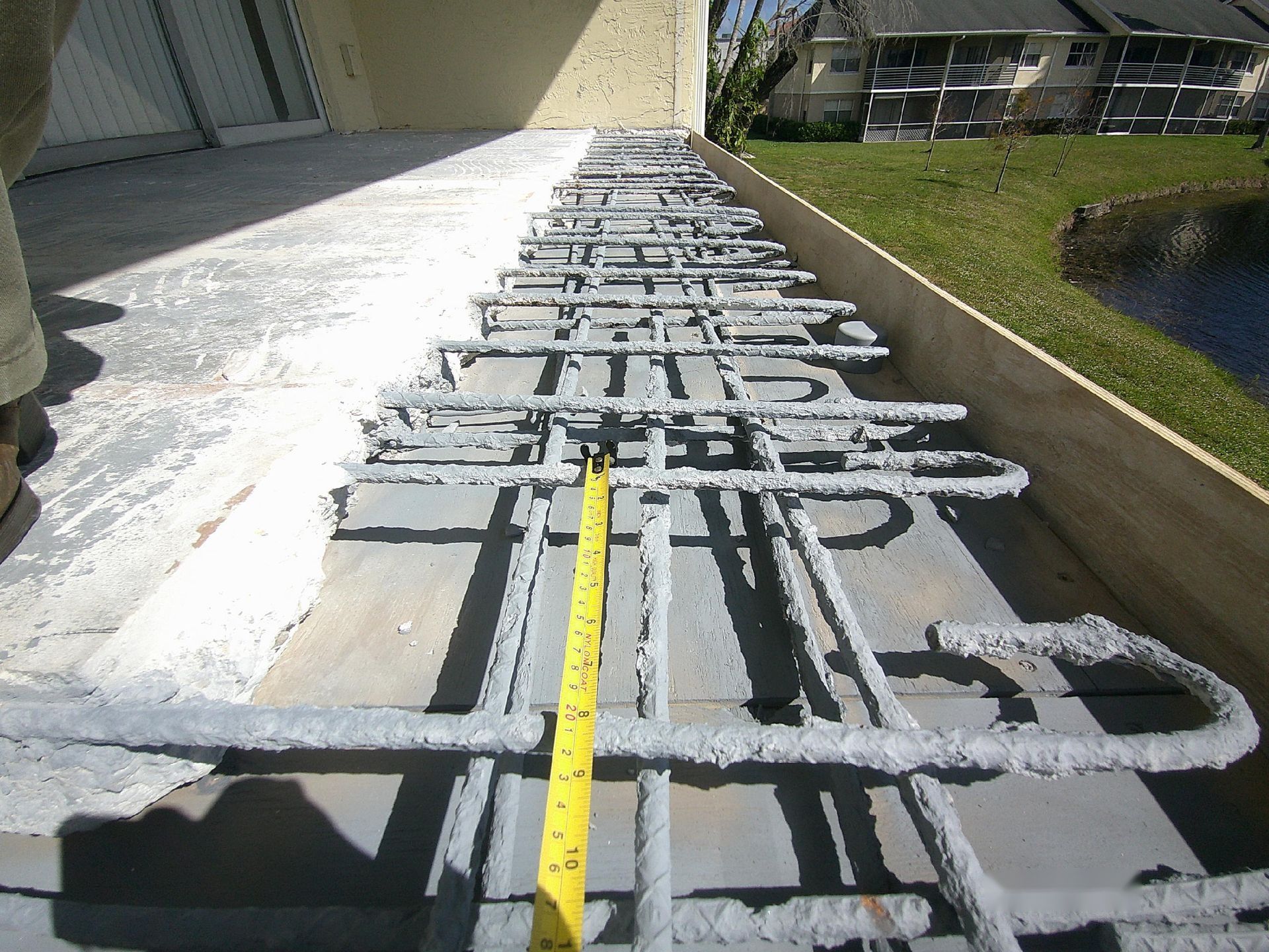 Balcony slab edge opened up with cleaned and coated reinforcing steel and a tape measure showing bar spacing