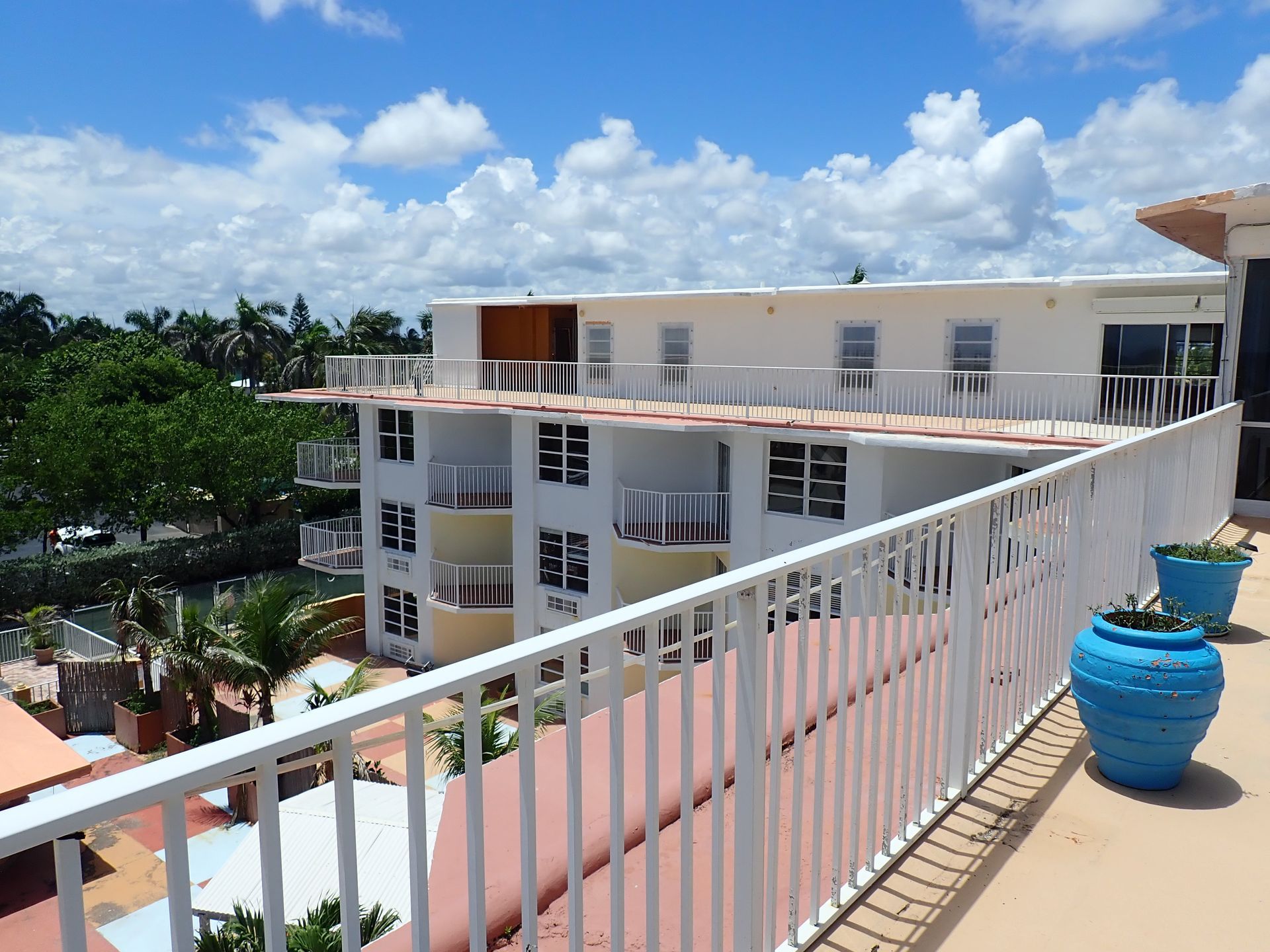 Rooftop terrace view overlooking a white and yellow condominium building's balconies and courtyard, with tropical landscaping in the background, during a milestone inspection by M&P Consulting Engineers
