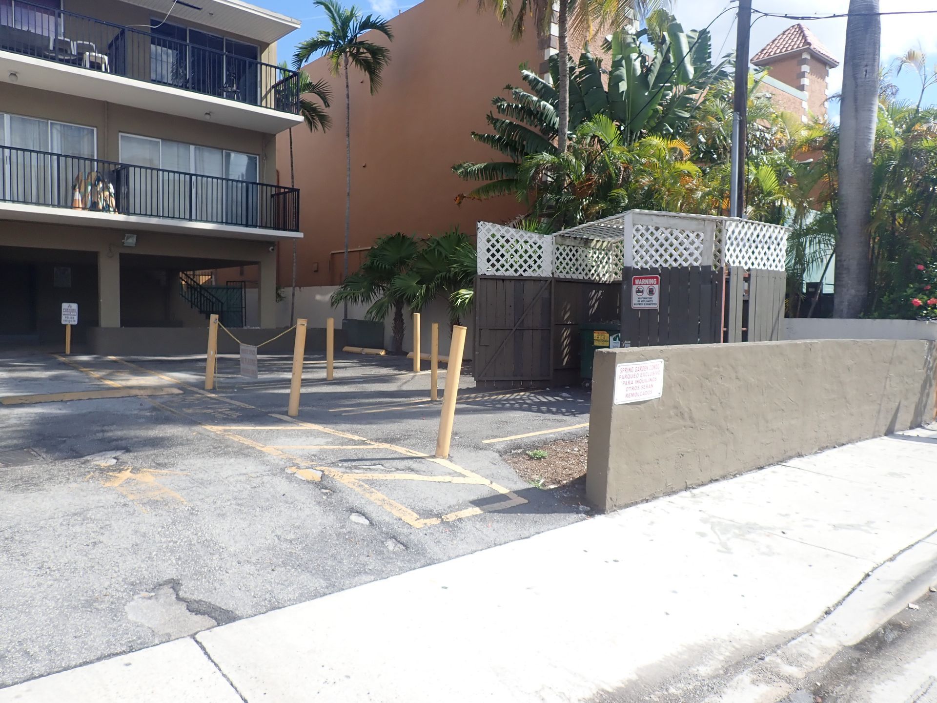 Parking lot and dumpster enclosure at Spring Garden Condo, with a wall-mounted 'Spring Garden Condo' parking sign and building exterior in the background, during a milestone inspection by M&P Consulting Engineers