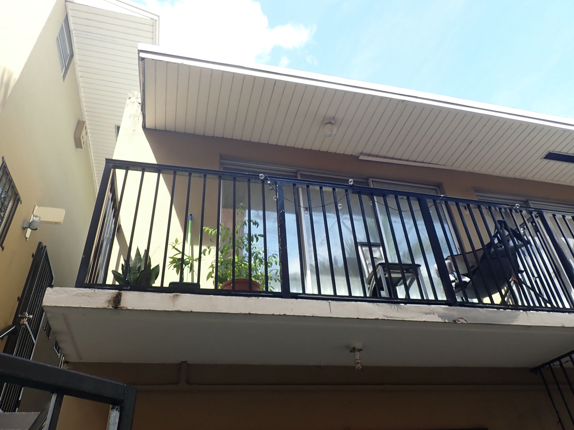 Exterior view of a second-floor balcony with metal railing, potted plants, and patio furniture during a milestone inspection by M&P Consulting Engineers