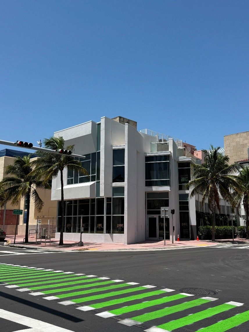 Modern corner building with glass windows and palm trees beside a crosswalk on a sunny street