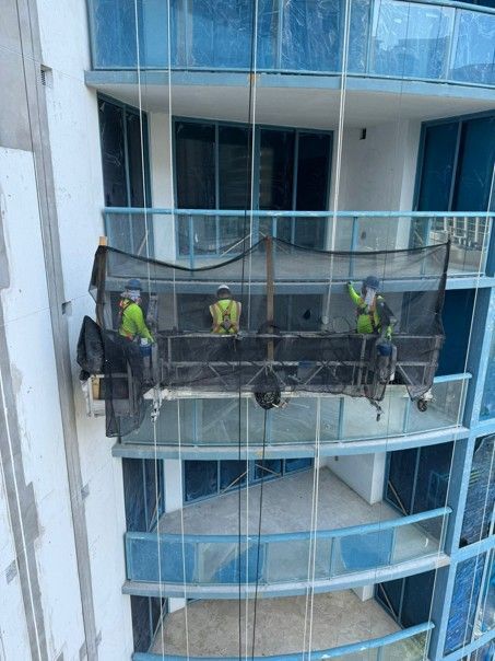 Workers in neon vests on a suspended scaffold repairing a high-rise building exterior