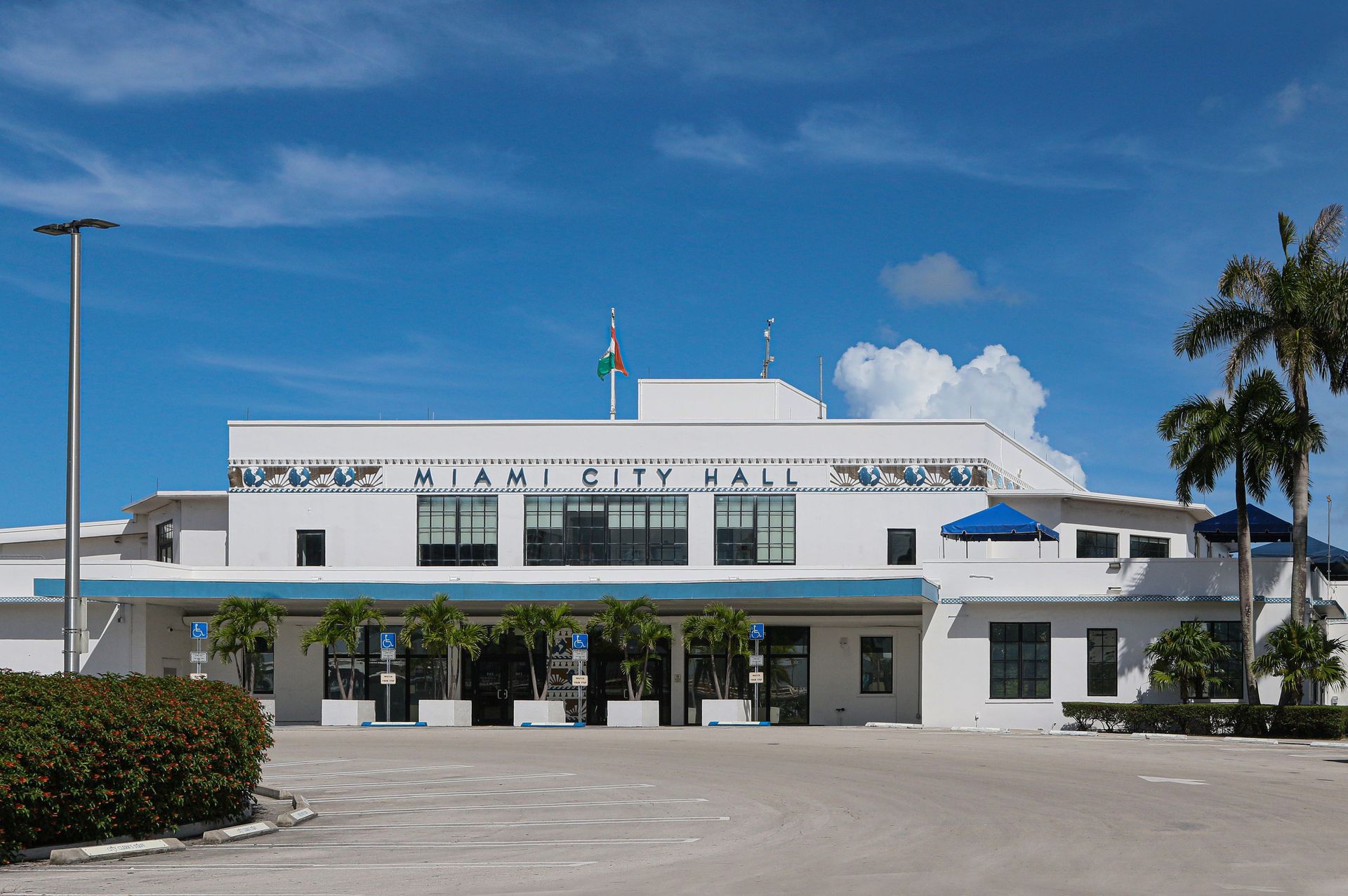 Front view of Miami City Hall under a blue sky, with palm trees and parking lot in front