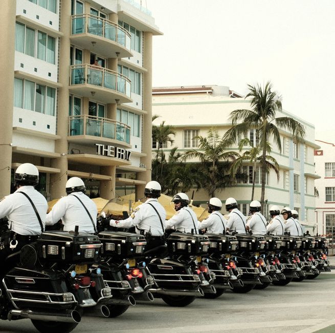 Police officers on motorcycles lined up on a city street beside apartment buildings