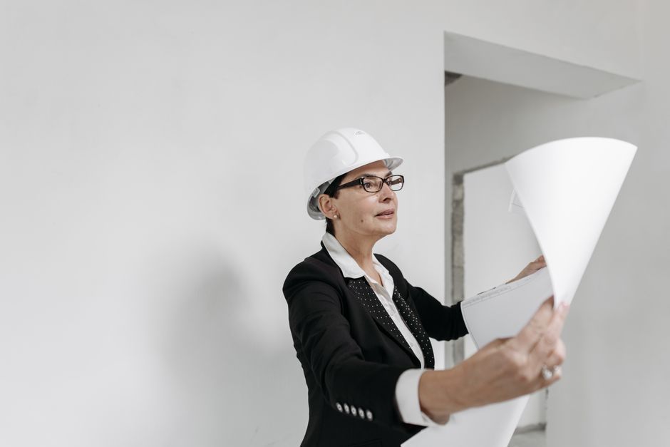 Architect in hard hat reviewing large blueprint indoors