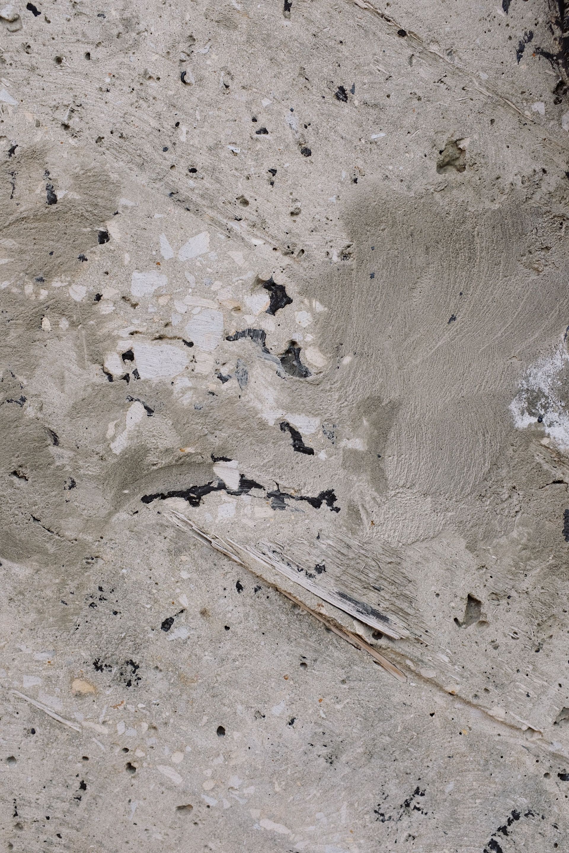 Close-up of weathered gray concrete with cracks, stains, and small white specks