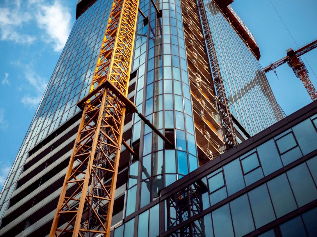 Glass high-rise under construction with a yellow tower crane against a blue sky