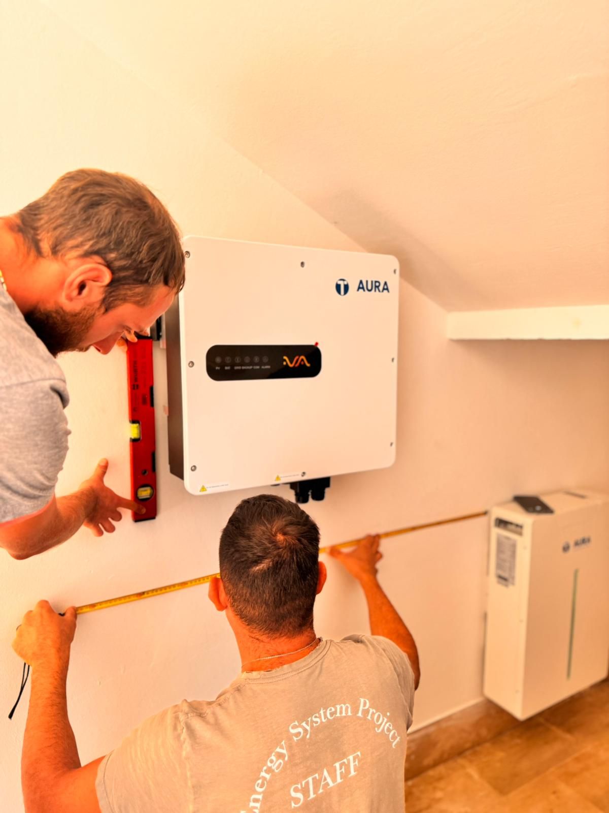 Due tecnici installano un inverter solare a parete in una stanza interna luminosa.