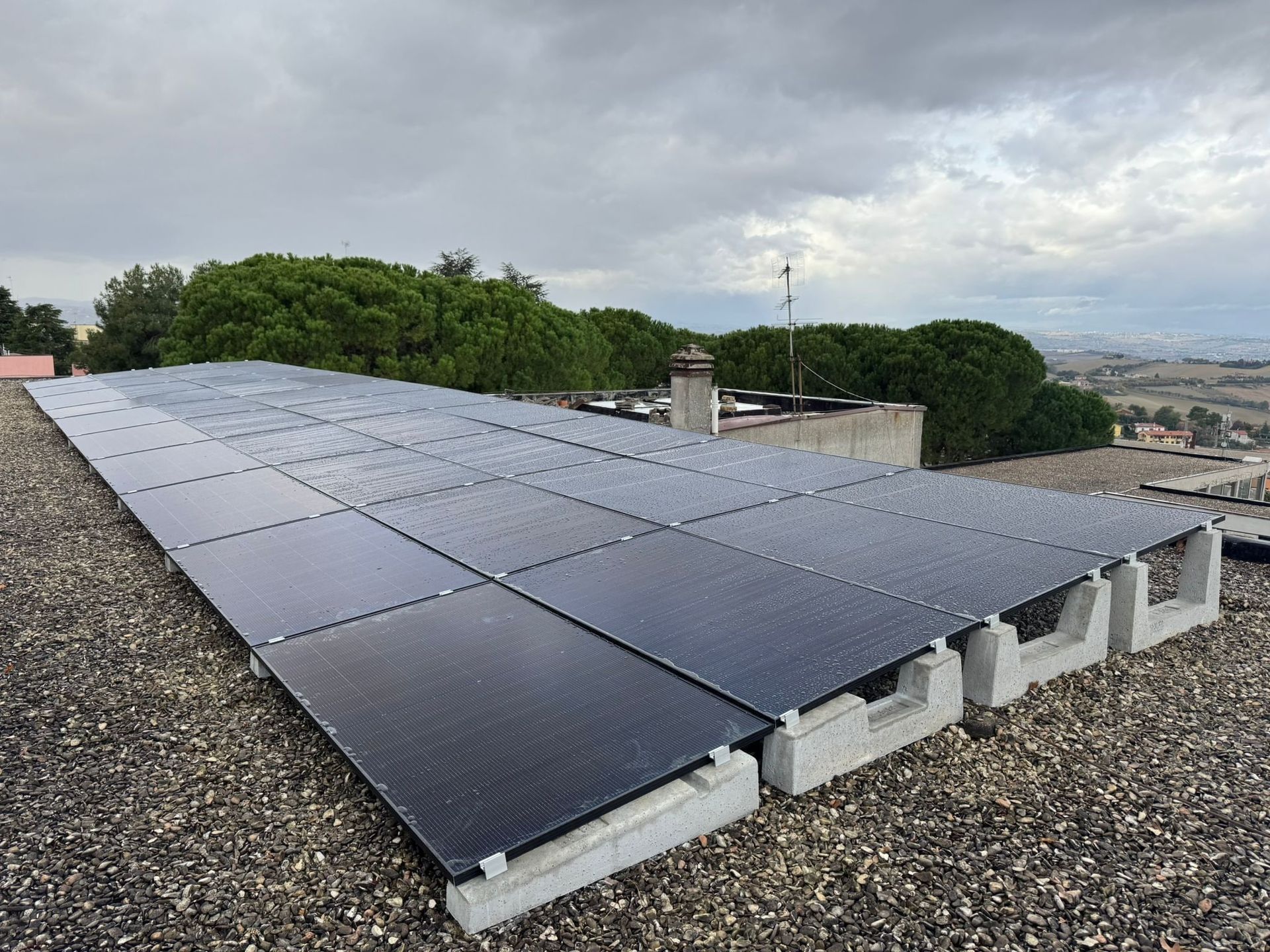 Pannelli solari installati su un tetto sotto un cielo nuvoloso, con copertura in ghiaia e colline sullo sfondo.