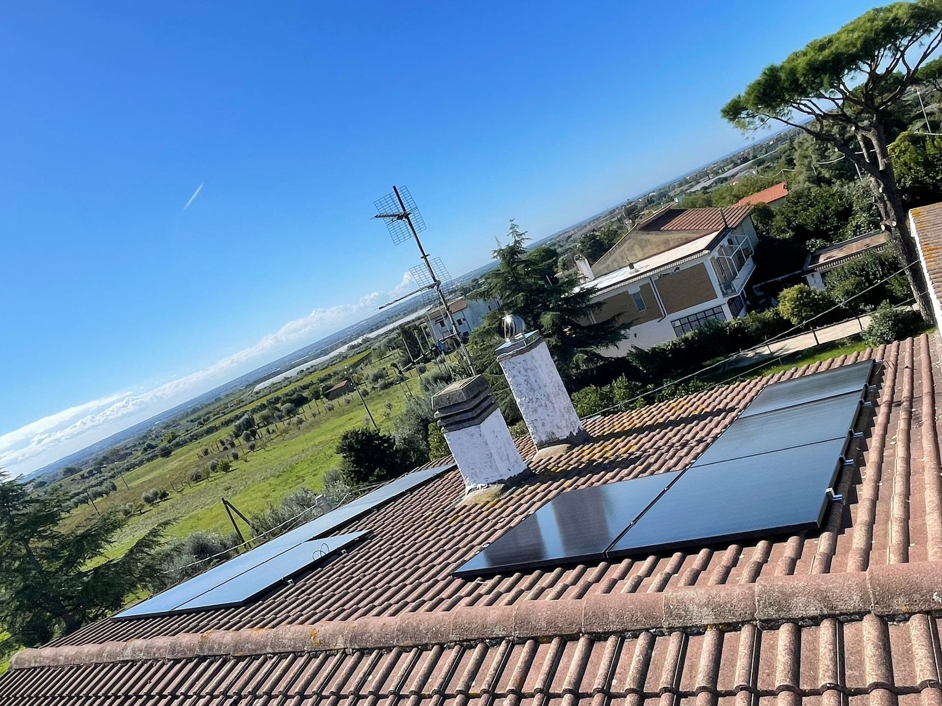 Pannelli solari sul tetto con vista su un paesaggio verdeggiante sotto un cielo azzurro e limpido.