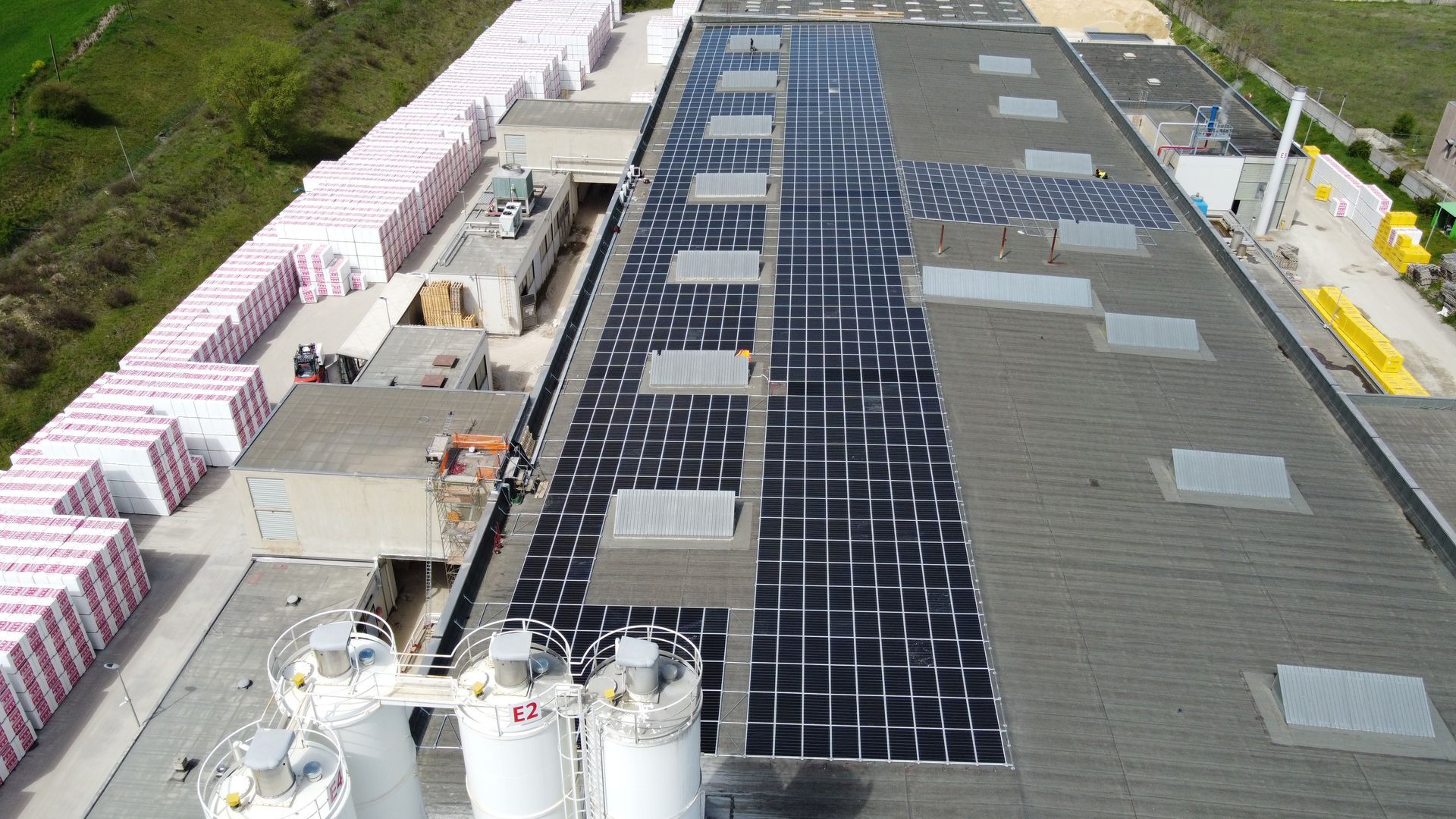 Cantiere edile con un grande tetto in fase di installazione e pile di materiali da costruzione a lato.