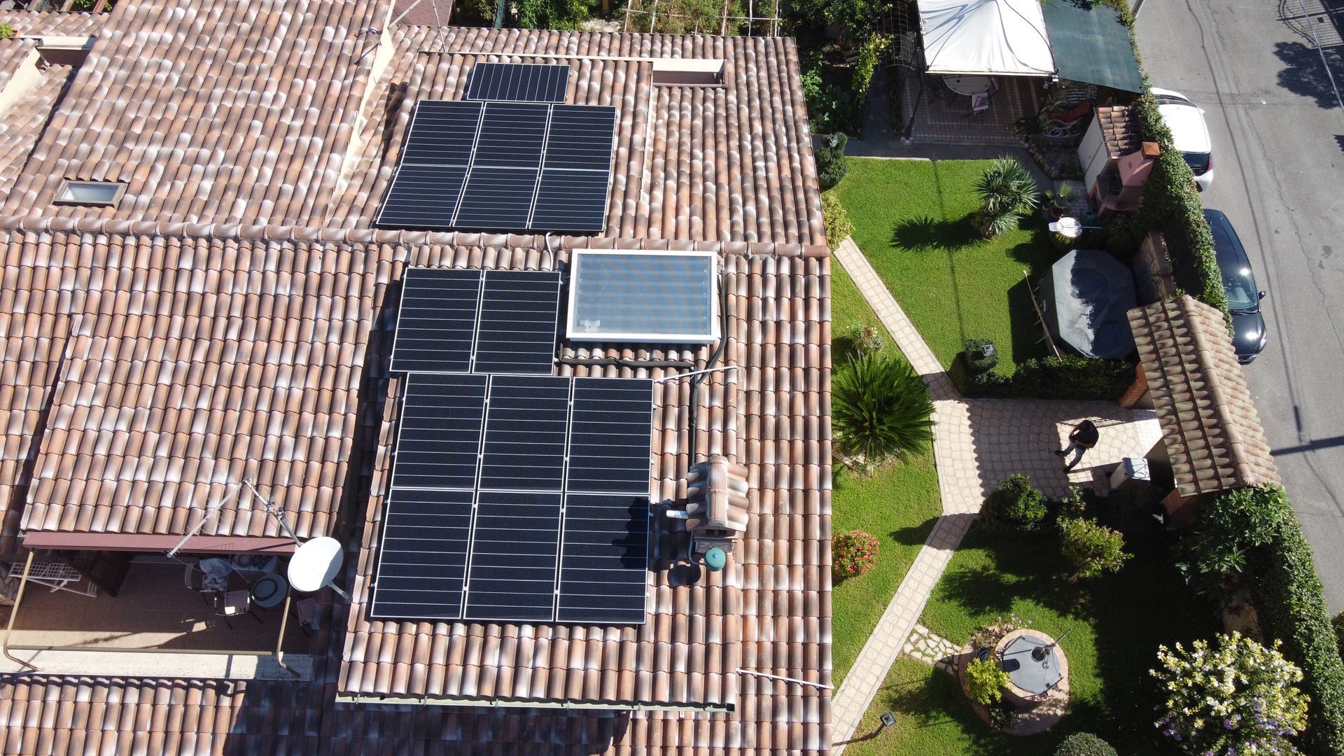 Veduta aerea di un tetto di tegole con pannelli solari accanto a un giardino verde e a un patio.