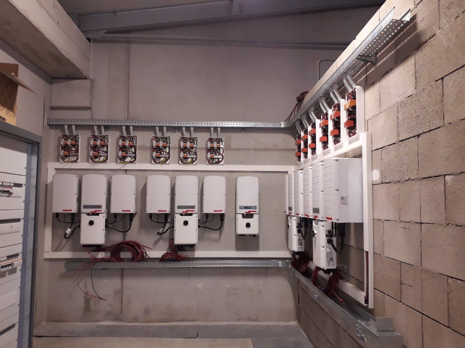 Pannelli elettrici e cablaggi montati su una parete di blocchi di cemento in un locale di servizio non rifinito.