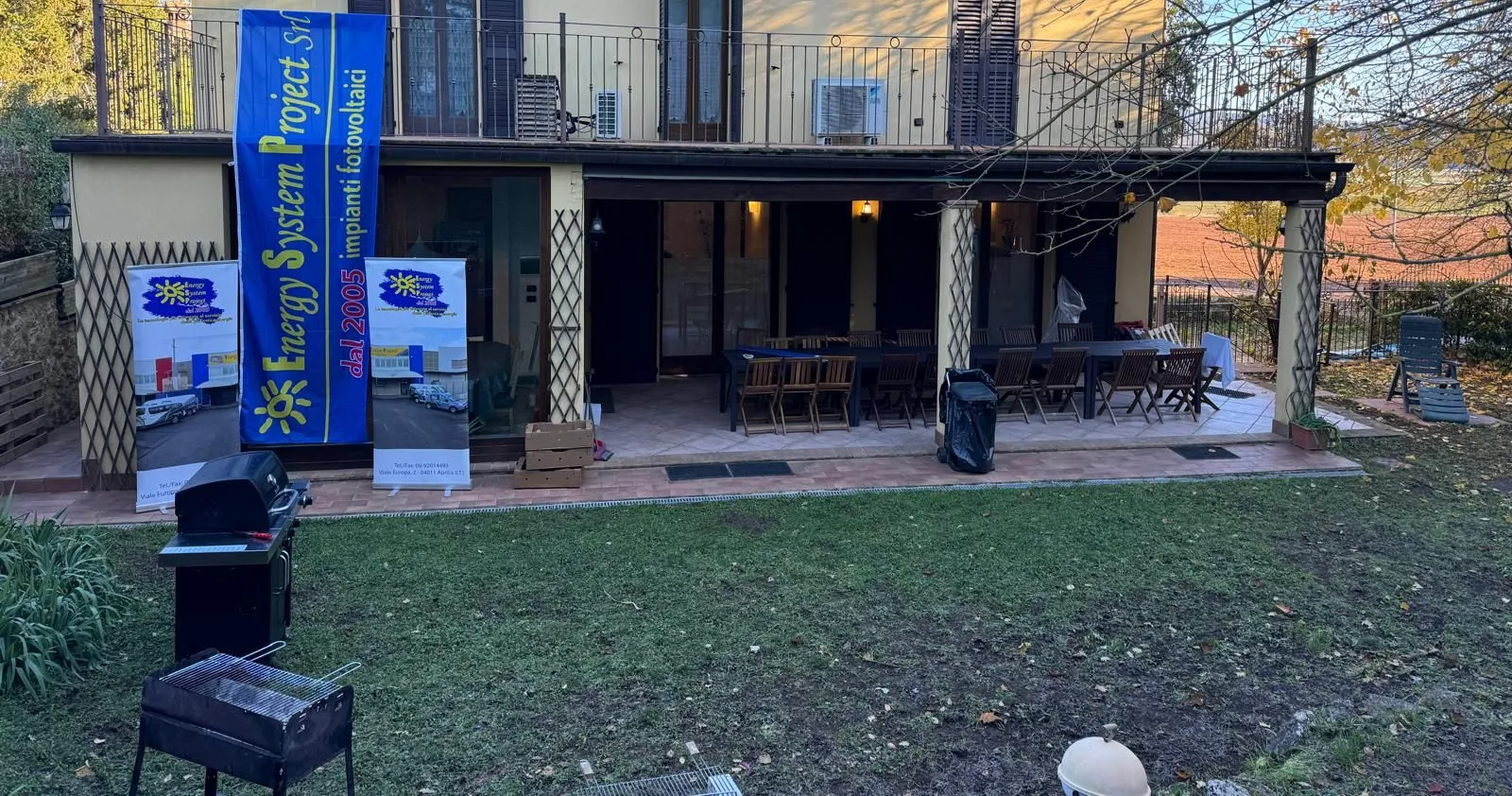 Patio esterno con tavoli, striscioni blu e un prato erboso di fronte a un edificio