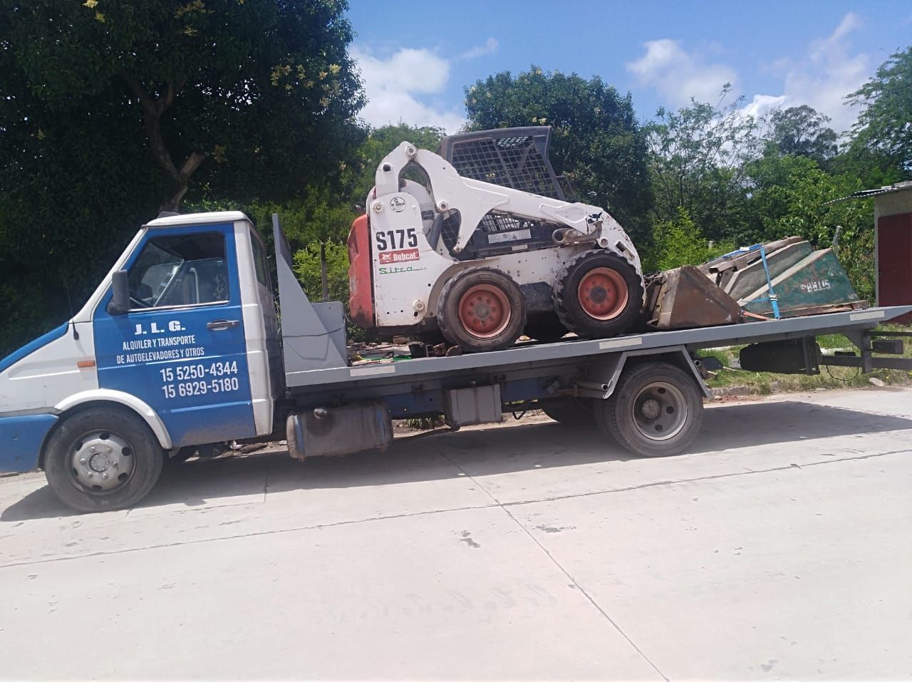 Una grúa con un bobcat en la parte trasera está estacionada al costado de la carretera.