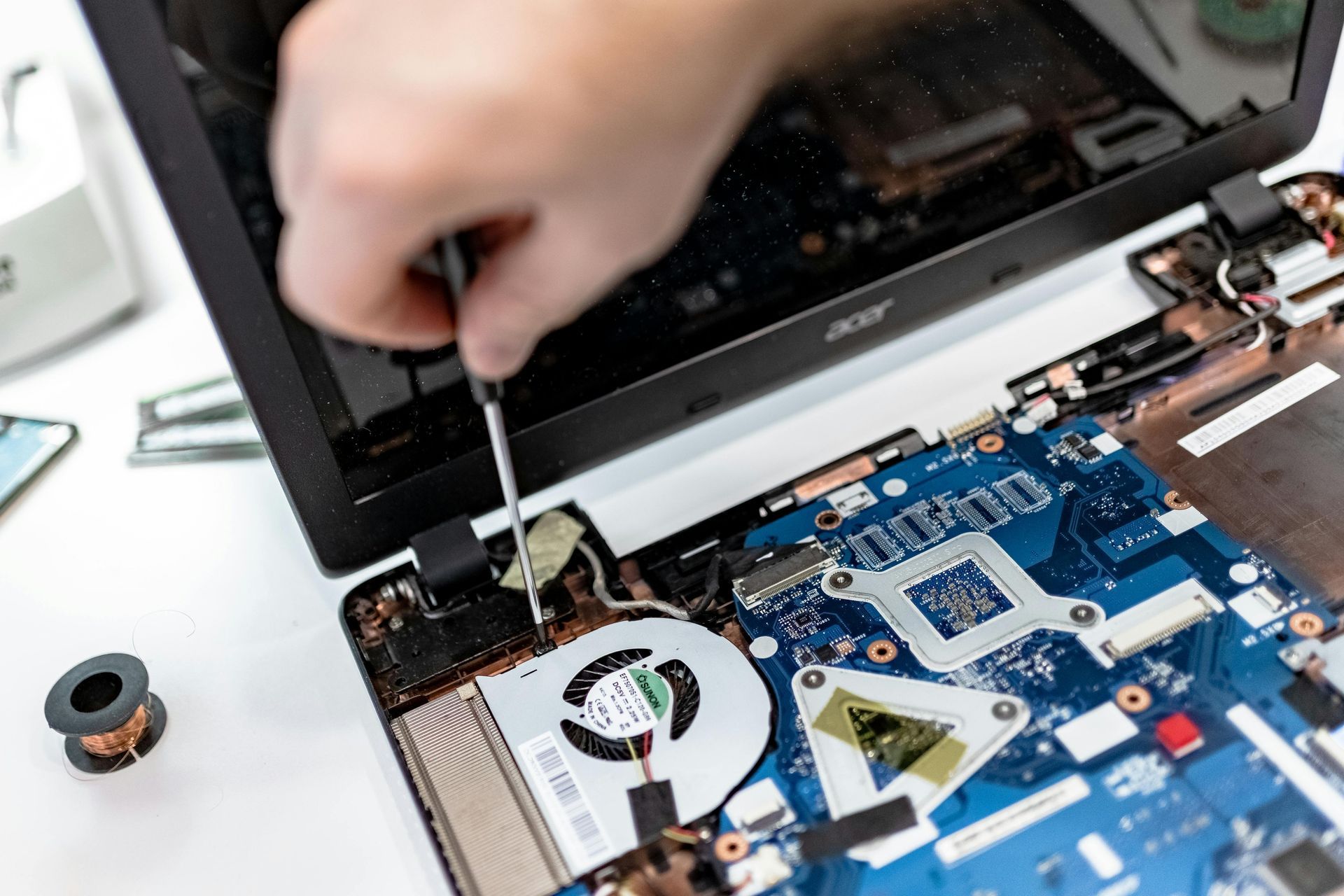Person repairing a laptop, using a screwdriver on the internal components with blue motherboard visible.