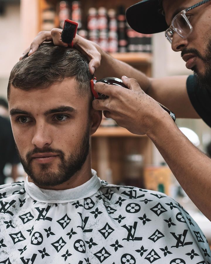 A Man is Getting His Hair Cut by a Barber Wearing a Louis Vuitton Cape — Barber Bros & Co - Southport in Southport, QLD